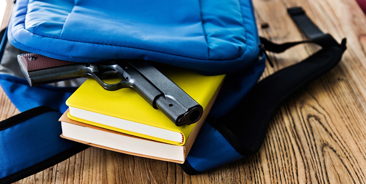 small gun sitting on yellow books sticking out of a backpack