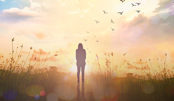 Silhouette of woman standing in a field with the sun behind her.