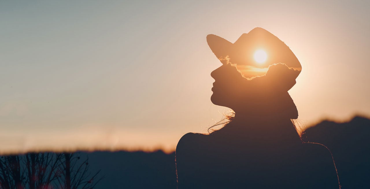 silhouette women wearing a hat looking at sunset and sun representing mental health