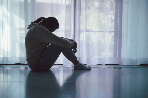teen girl sitting on floor with head down in front of a window