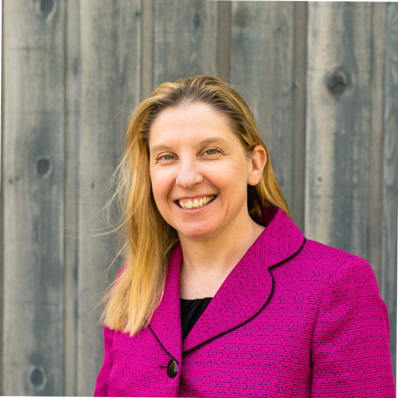 woman in pink blazer coat in front of wood wall